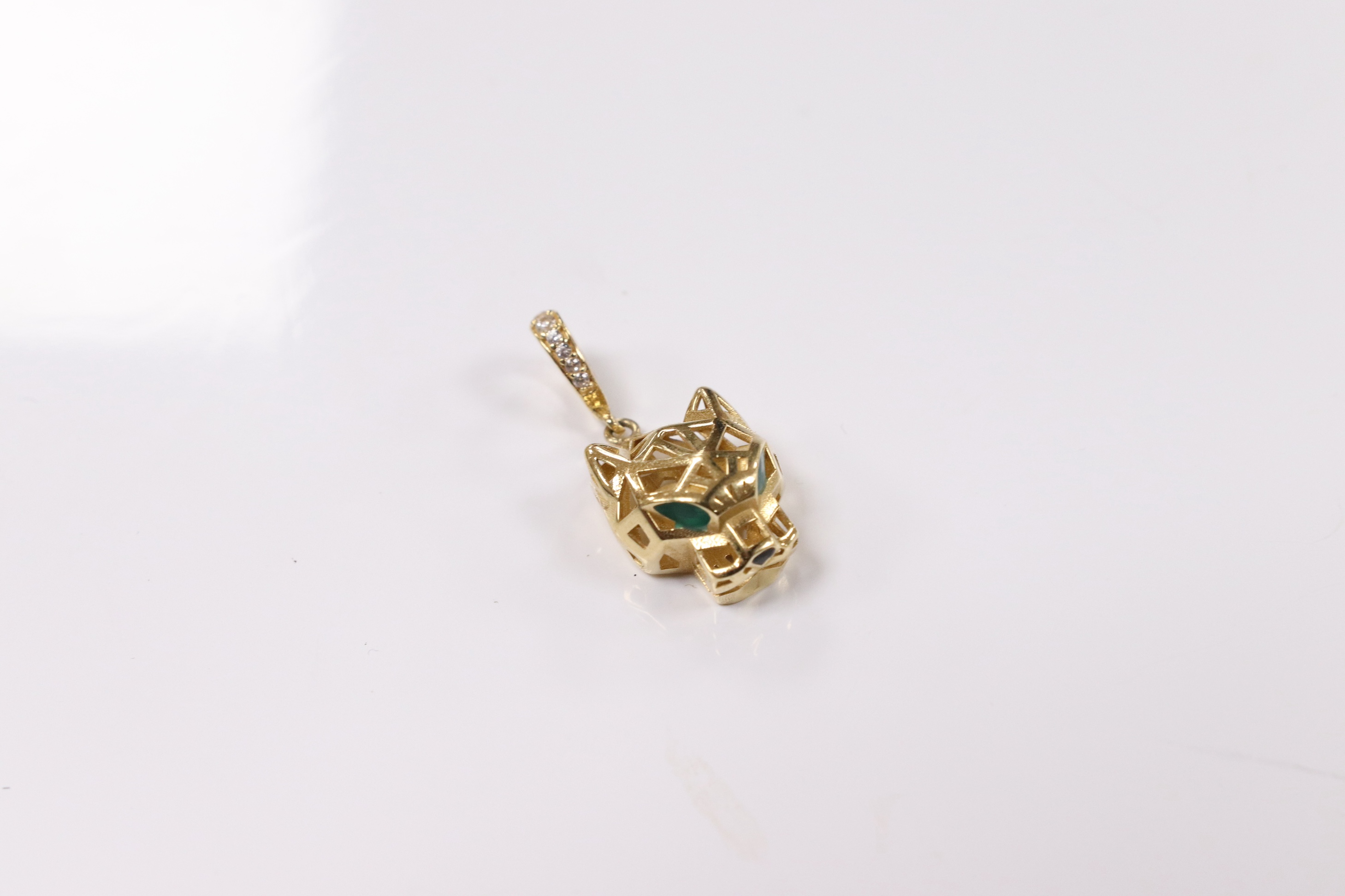 A modern Cartier style pierced 18k and emerald? set pendant, modelled as a leopard's head, with diamond chip set bale, overall 27mm, gross weight 2.5 grams. Condition - fair